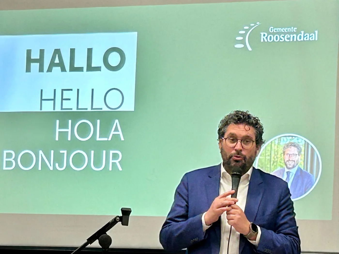 Arwen van Gestel spreekt bij een presentatie met Hallo, Hello, Hola en Bonjour op het scherm